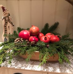 a bowl filled with pomegranates and pine cones on top of a counter