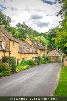 an empty street lined with stone houses in the country side, surrounded by lush green trees and bushes