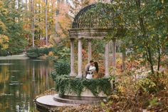 a bride and groom kissing in front of a gazebo surrounded by trees with fall foliage