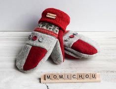 two red and gray mittens sitting next to scrabble letters on a white surface