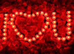 the word love spelled with lit candles in front of red flowers and petals on a black background