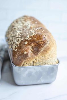 a loaf of bread sitting in a tin on top of a white countertop next to a knife