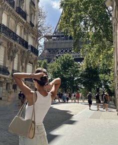 a woman standing in front of the eiffel tower with her hand on her head