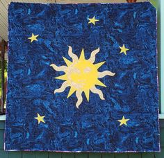 a blue quilt with yellow stars and the sun on it is hanging from a porch