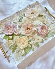 a glass tray with flowers on it sitting on a white cloth covered tablecloth,