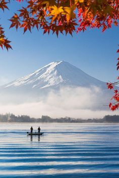 two people on a boat in the water with a mountain in the background