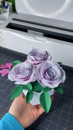 someone is holding some paper flowers in front of a printer machine with it's lid open