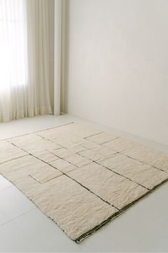 a white room with a large rug on the floor and curtains in the window behind it