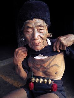 an old man with tattoos on his face and chest sitting in front of a mirror