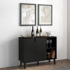 two framed pictures hang on the wall above a black cabinet with wine glasses and bottles