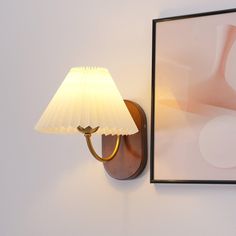 a lamp is on the wall next to a framed photograph and a light fixture with a white shade