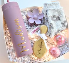 a pink and gold gift box filled with personalized items, such as a cup, spoons, cookies, and more