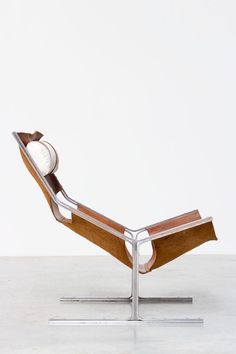 a wooden and metal lounge chair sitting on top of a white floor next to a wall