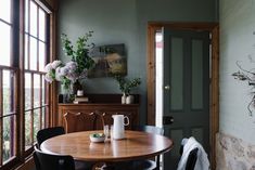 a wooden table sitting in front of two windows next to a doorway with potted plants on it