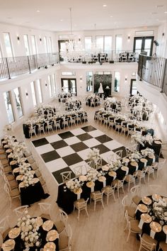 an indoor wedding reception setup with black and white checkerboard flooring, chandeliers and tables