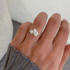 a woman's hand wearing a gold ring with two pear shaped diamonds on it