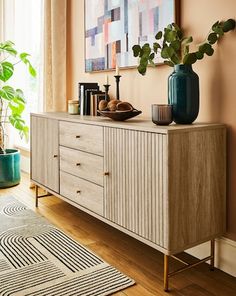 a living room with a large painting on the wall next to a dresser and potted plant