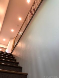 a stair case with wooden handrails next to a white wall and light fixture