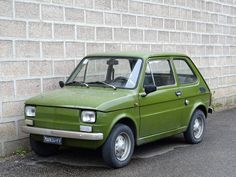 an old green car parked in front of a brick wall