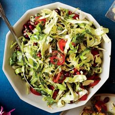 a bowl filled with lettuce, tomatoes and other food on top of a blue table