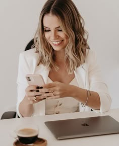 a woman sitting at a table looking at her cell phone and holding a coffee cup