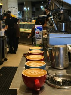 three cups of coffee sit on the counter next to two espresso machines in a restaurant