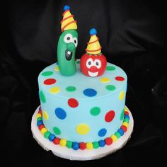 a birthday cake decorated with colorful polka dots and an odd face on top, sitting on a black background