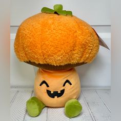 an orange stuffed animal with a pumpkin on it's head, sitting in front of a white wall