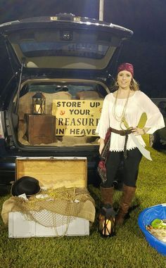 a woman standing in front of an open trunk filled with items on the grass next to a car