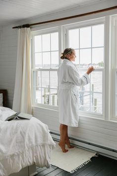 a woman in a bathrobe standing by a window looking out at the water