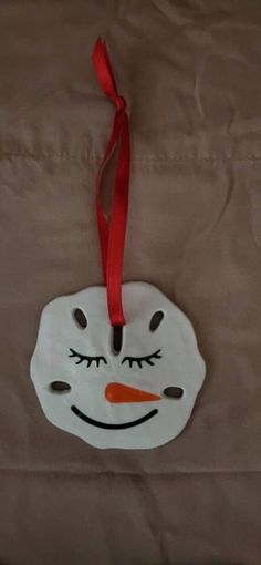 a snowman face ornament hanging from a red ribbon on a brown sheet