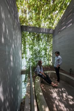 two people sitting on concrete benches in a courtyard area with greenery covering the ceiling