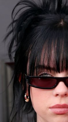 a close up of a person wearing sunglasses with hair in the air and piercings on their ears