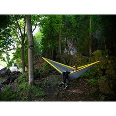 a woman sitting in a hammock with trees and rocks behind her on the ground