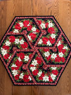 a quilted table top with poinsettis and flowers on it, sitting on a wooden surface