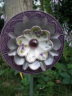 a purple and white flower shaped dish on top of a metal stand in the grass