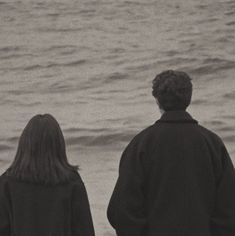 two people standing on the beach looking out at the water