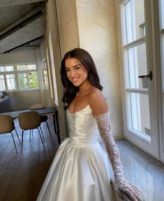 a woman in a white wedding dress standing next to a window with her hand on the wall