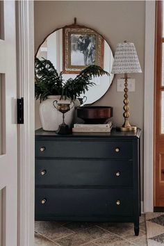 a dresser with a mirror, lamp and plant on it in front of a door