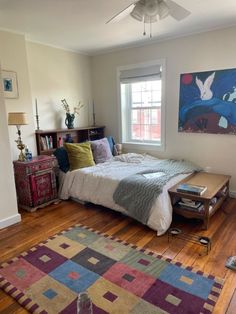 a bedroom with a bed, dresser and rug on the wooden floor in front of a window