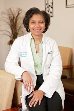 a woman in a white lab coat sitting on a chair with her hand on her knee