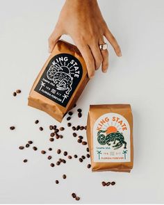 two bags of coffee sitting next to each other on top of a white table with beans scattered around them