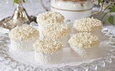 four cupcakes with white frosting sitting on a glass platter next to a teapot