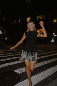 a woman standing in the middle of a crosswalk at night with her arms up