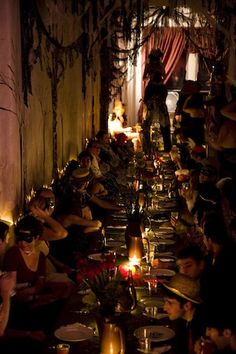 a group of people sitting at tables with candles in front of them and one person standing on the table