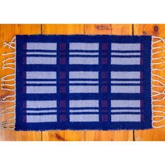 a blue and white rug with fringes on top of a wooden floor next to a wall