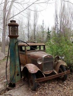 an old rusted out car sitting in the woods next to a light pole and tree