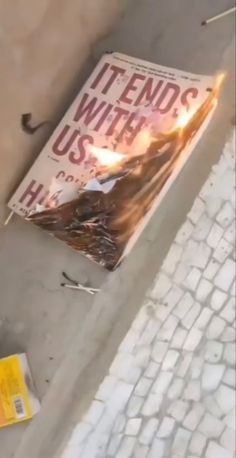 a protest sign laying on the ground next to a brick wall with a fire coming out of it