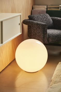 a white light sitting on top of a wooden floor next to a chair and book shelf