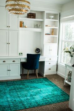 a blue rug in the middle of a room next to a desk and chair with a chandelier above it